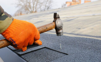 Image of a worker hammering a nail into a roof shingle