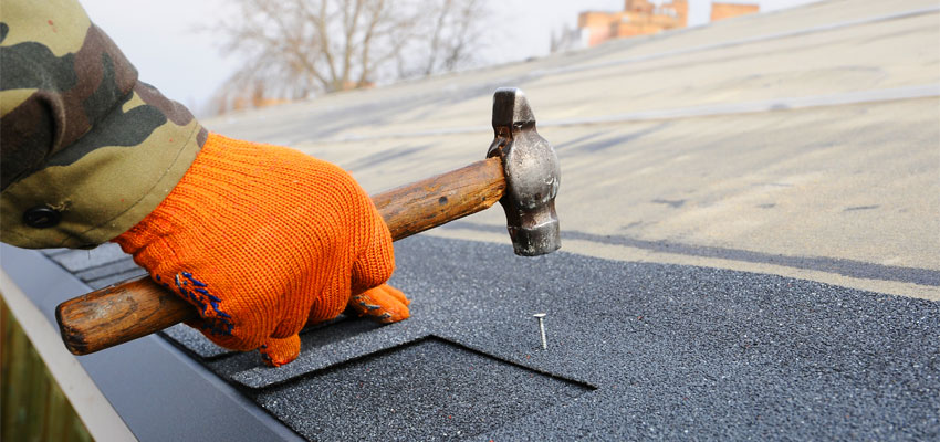 Image of a worker hammering a nail into a roof shingle